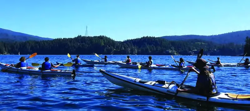 Students kayaking on the water near mountains during an outdoor education activity.