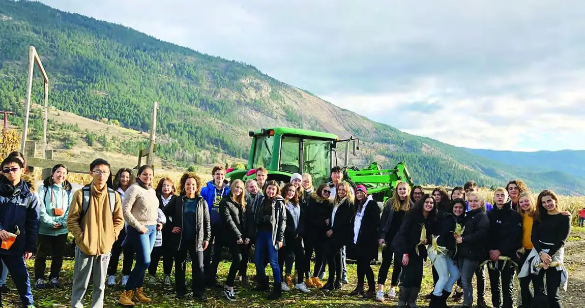 A large group of international students on a farm excursion with mountains behind.