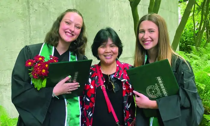 Graduating students in gowns holding diplomas and flowers with a staff member.